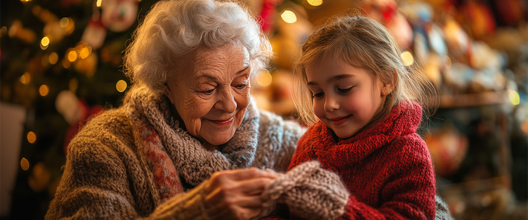 An older woman with her granddaughter in front of a christmas tree smiling.